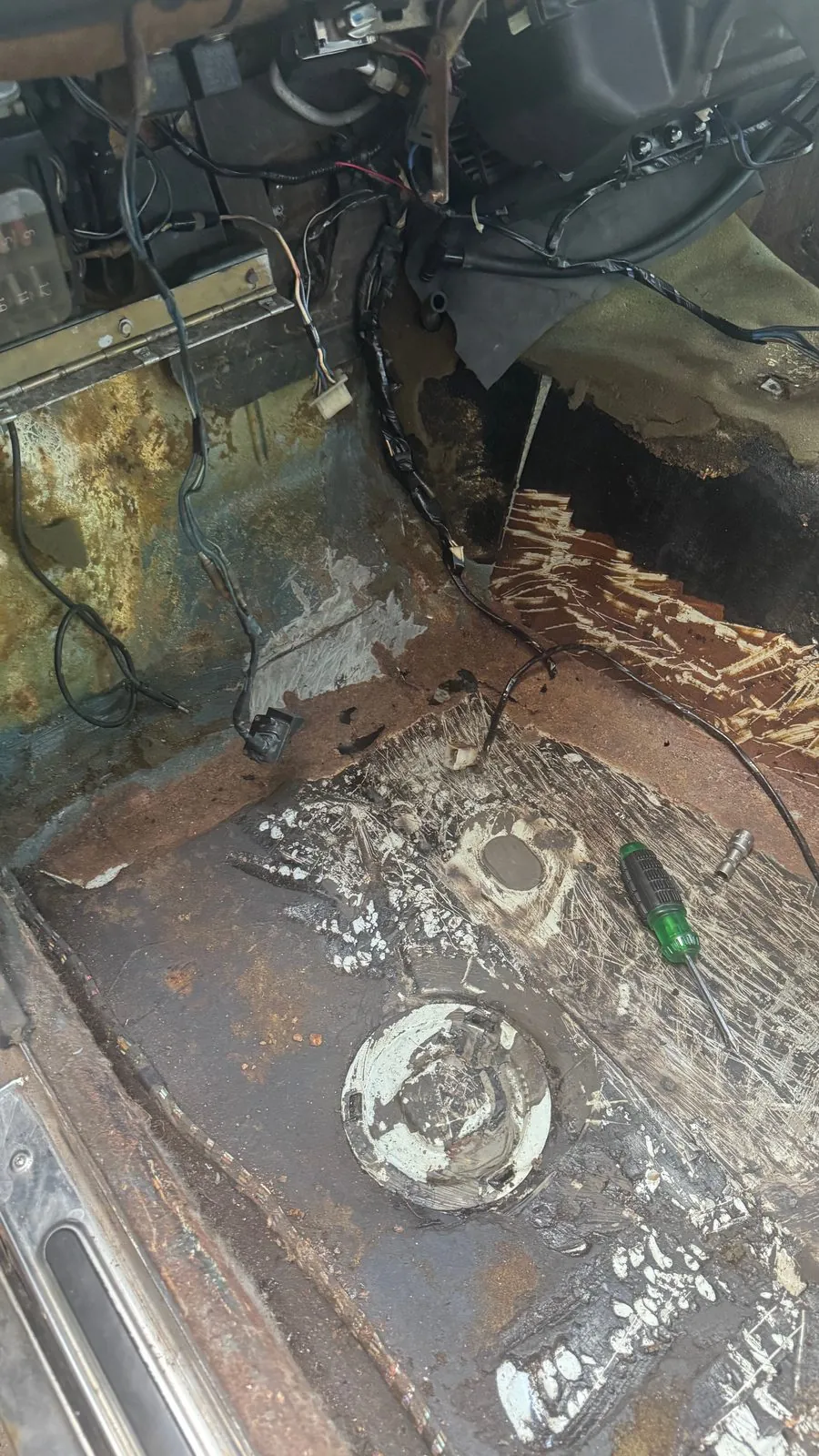 Stripped cabin floor of the old BMW with rust, loose wiring and old paint patches