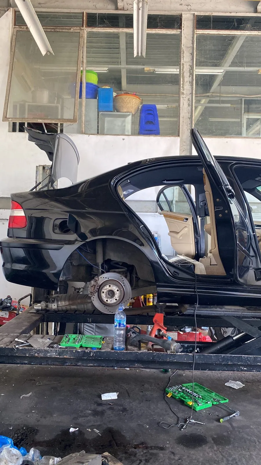 Black E46 on a lift, rear wheel off, interior stripped with cream seats, tools on the floor