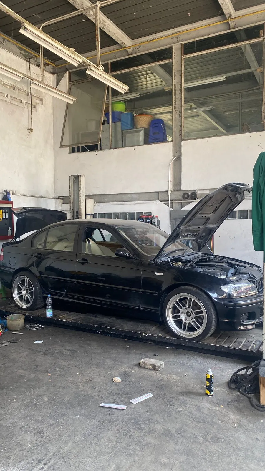 Black E46 on a lift in the workshop with bonnet raised, other engine parts on stands left of the car
