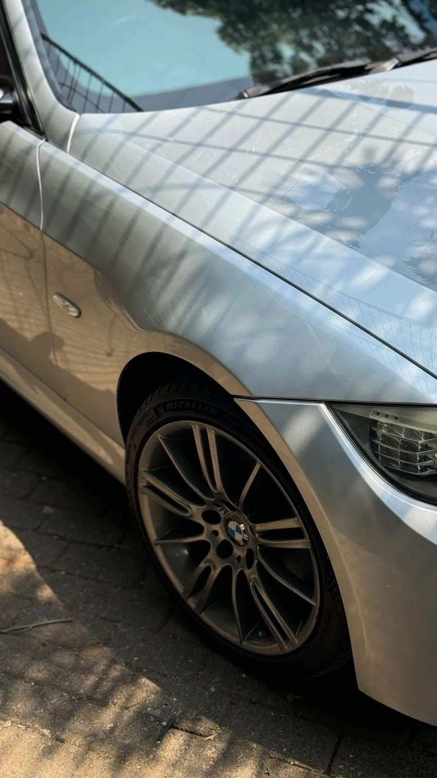 Silver E90 front wing and star-spoke wheel after paint, sun on the cobbles