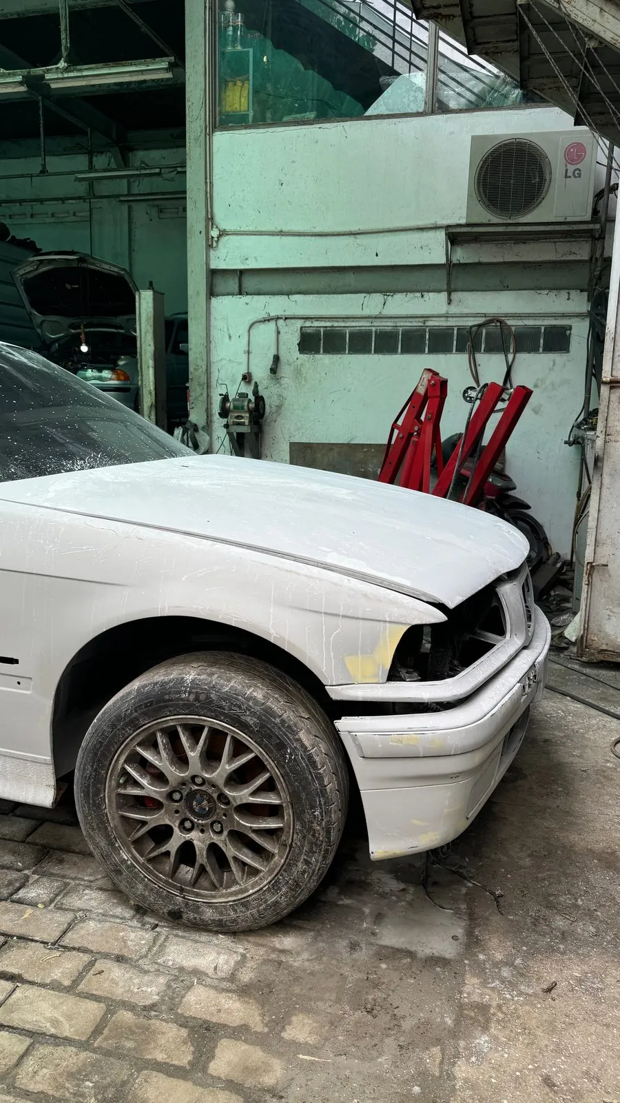Front wing and BBS-style wheel of the white-primed E36 with the headlight removed