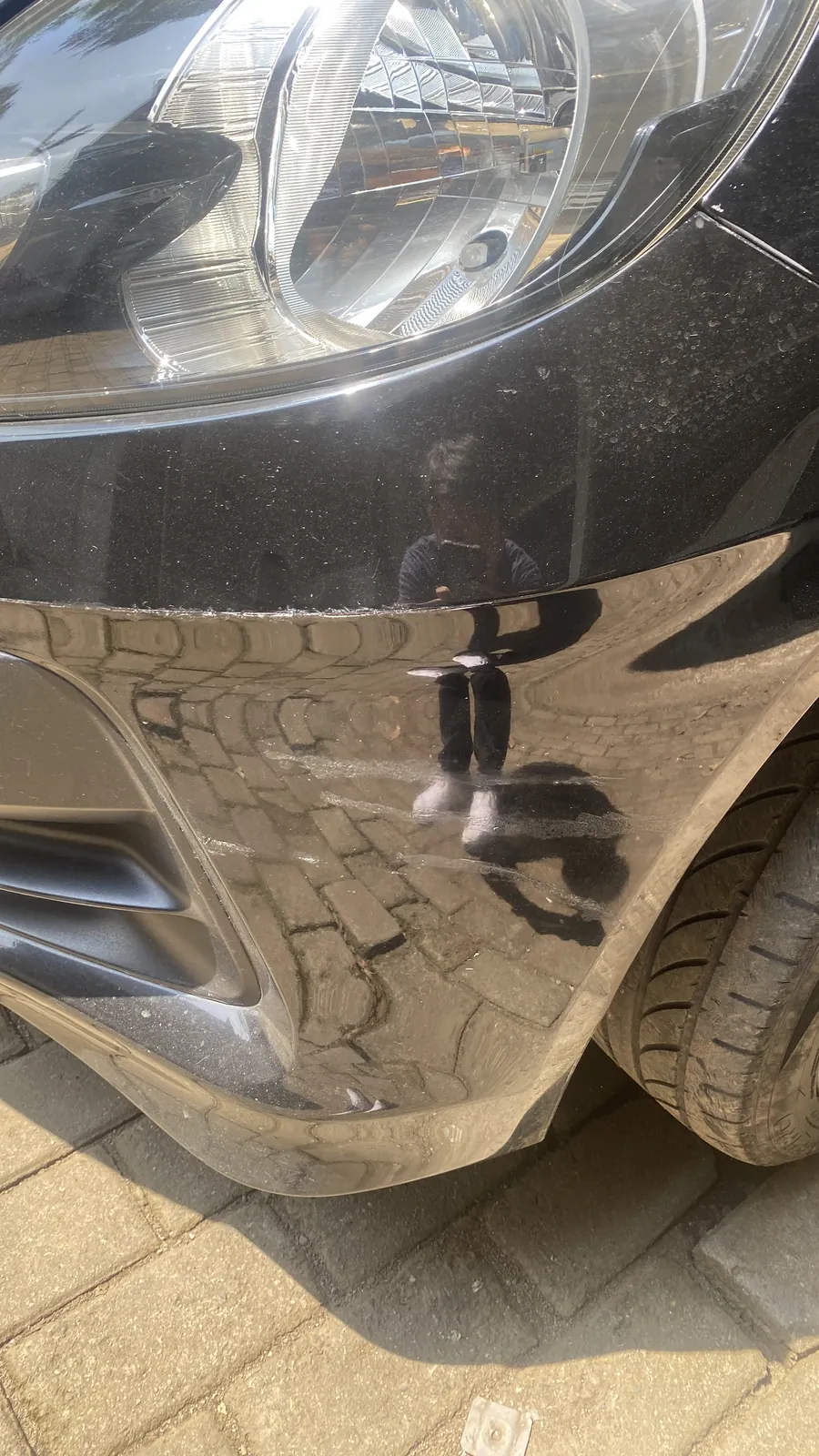 Scuffed front bumper of a black Honda Brio before the repair