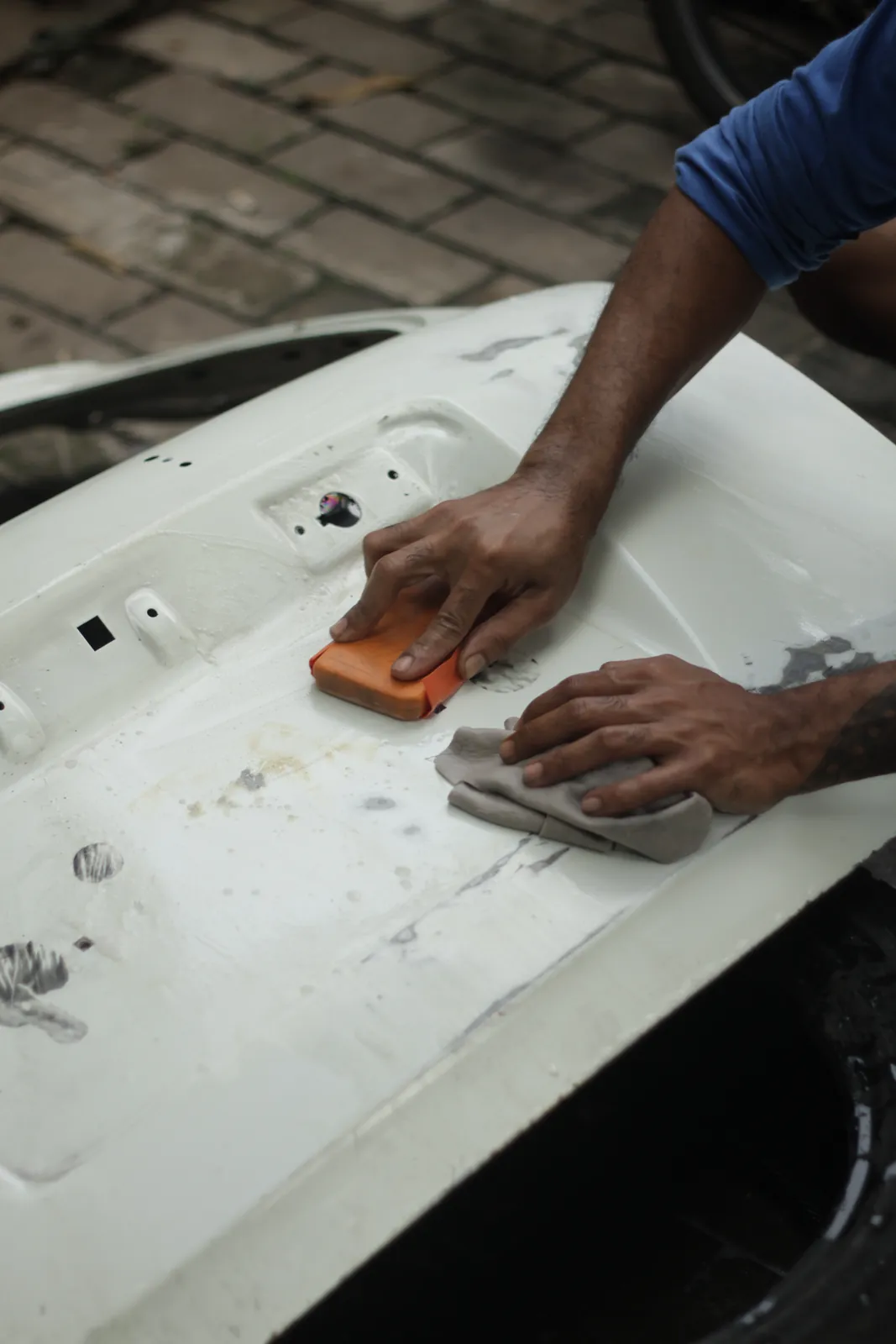 Two hands sanding a white tailgate with an orange block