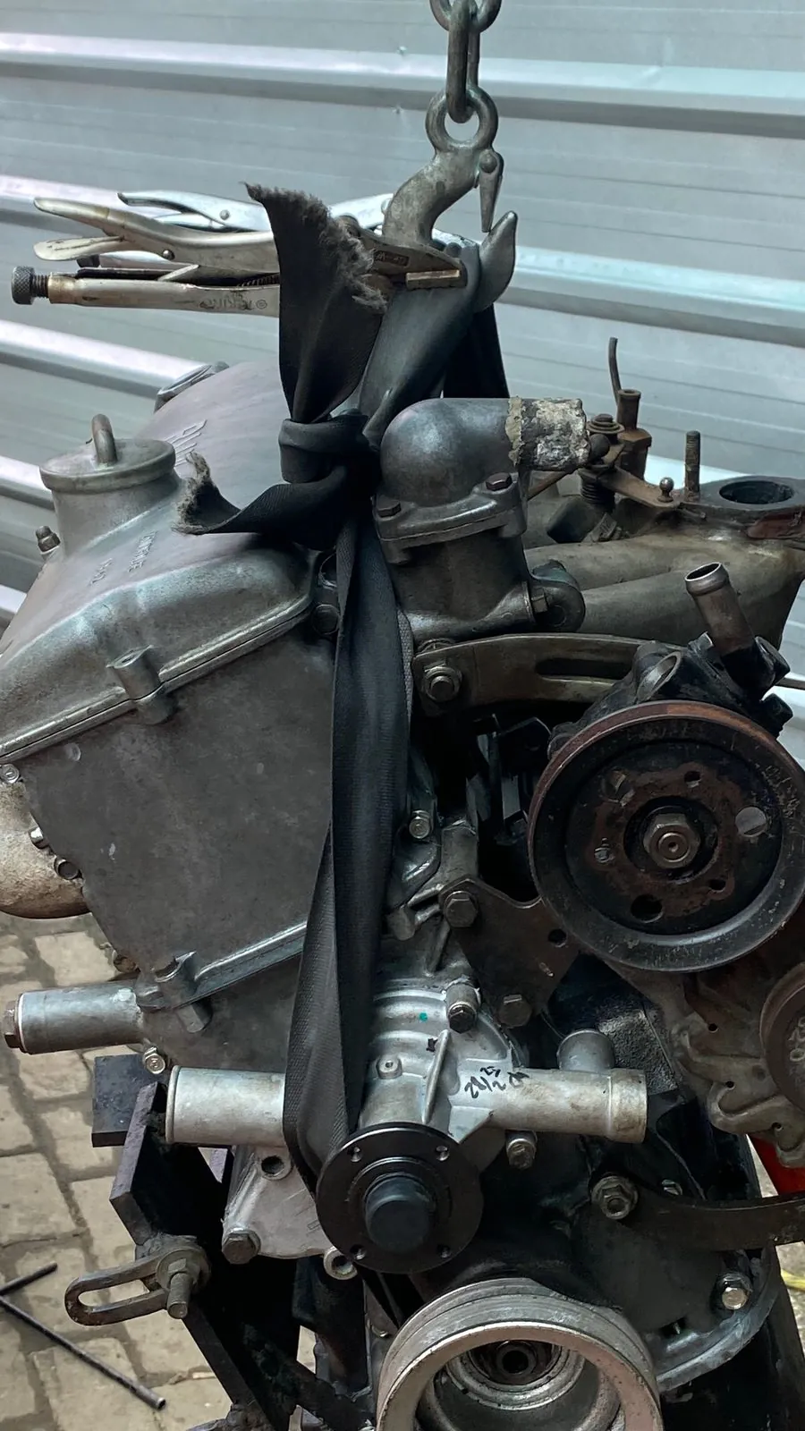 Old BMW four-cylinder engine lifted on a chain hoist, ancillaries on