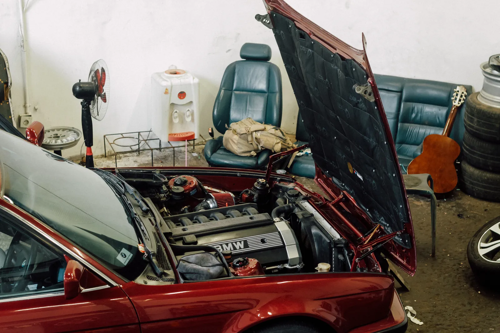 Maroon BMW E34 with the bonnet up inside the workshop