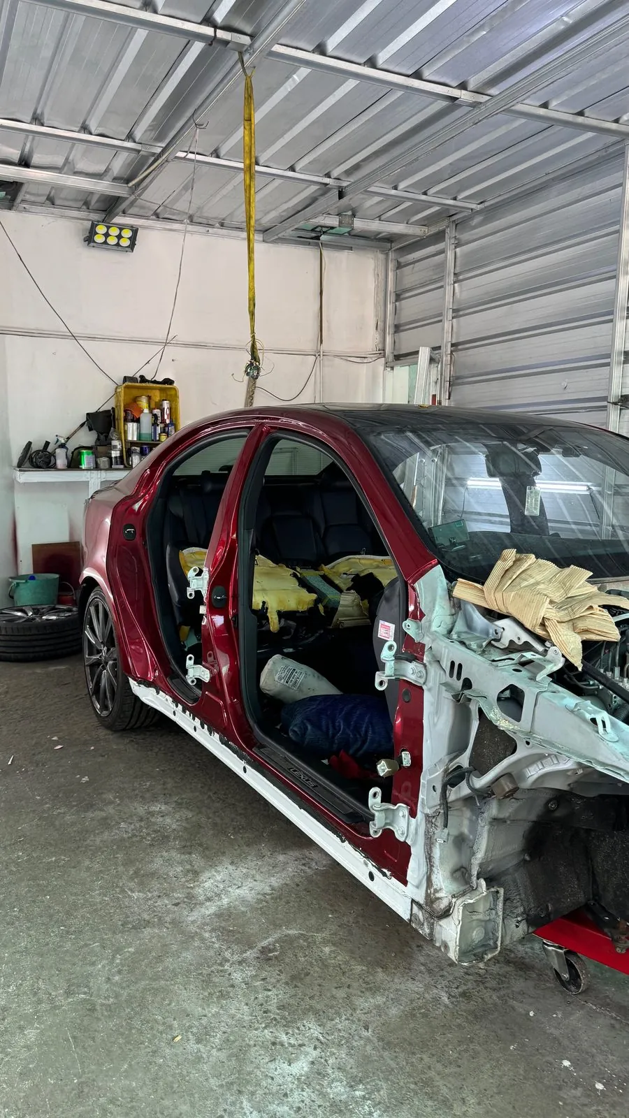 Stripped Lexus shell in red and white, doors open, front end off, glove on the sill, spray booth