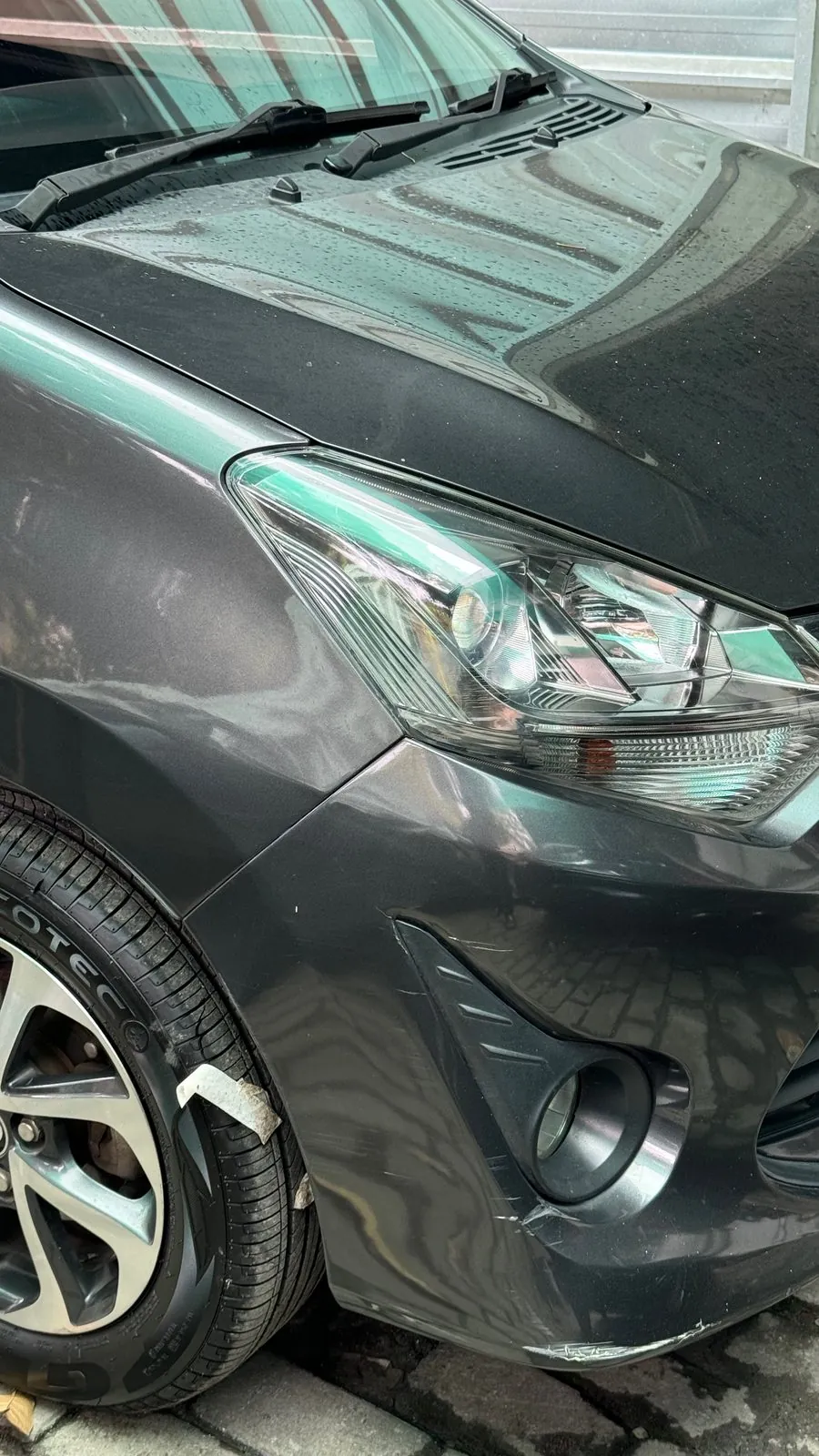 Scraped front bumper corner and wing above the fog lamp of a grey Toyota Agya