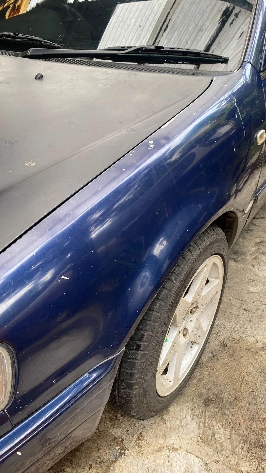 Oxidised faded bonnet and blue front wing of an old Toyota Corolla, alloy wheel